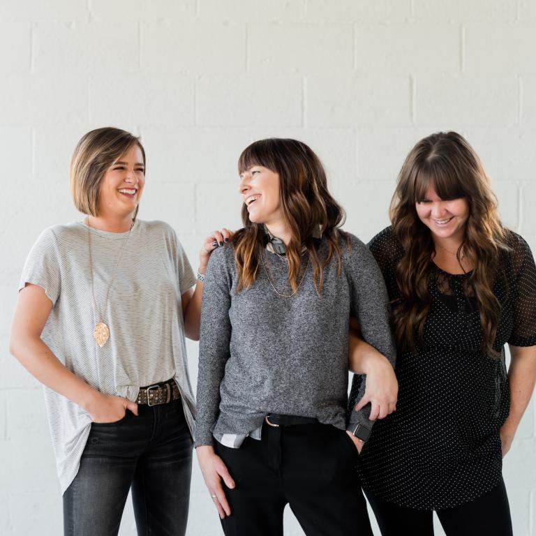 Drei jüngere Frauen stehen lässig nebeneinander und lachen.