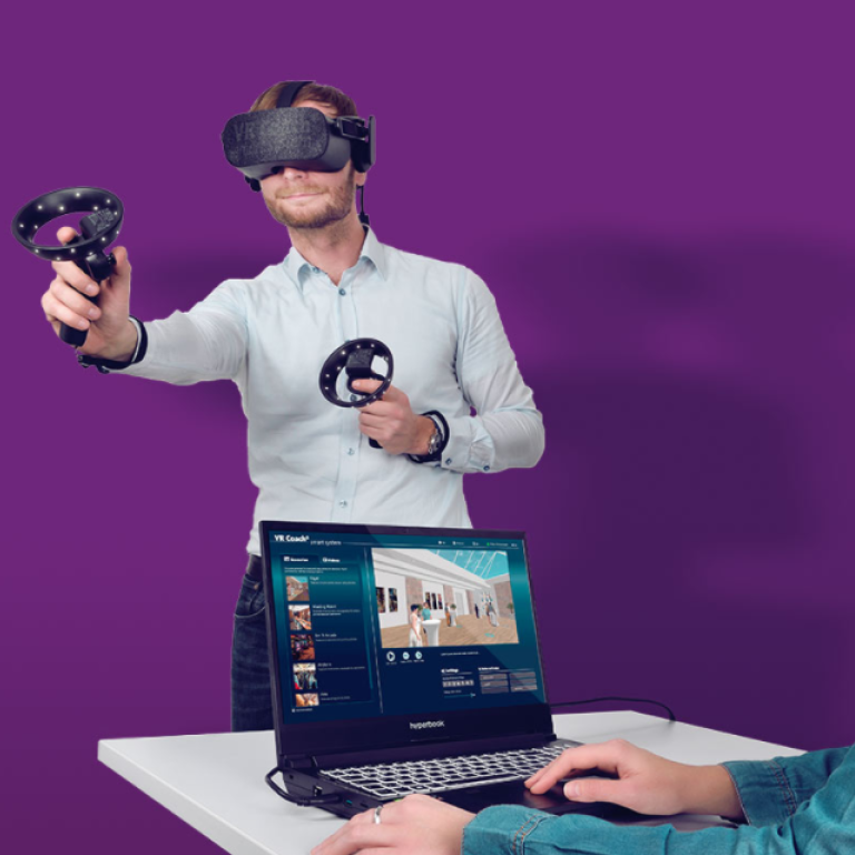 Vor einem lilafarbenen Hintergrund steht ein Mann mit VR-Brille und weiteren Utensilien in der Hand. Im Vordergrund sitzt eine Frau an einem Laptop und betreut die Situation.
