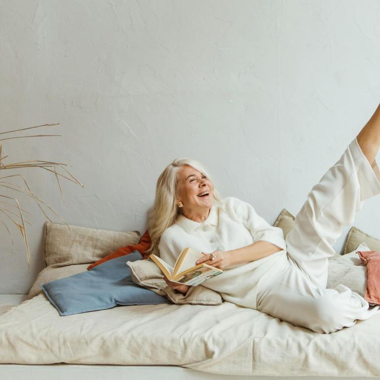 Eine ältere Frau liegt lächelnd auf einem Sofa und streckt ein Bein in die Höhe.