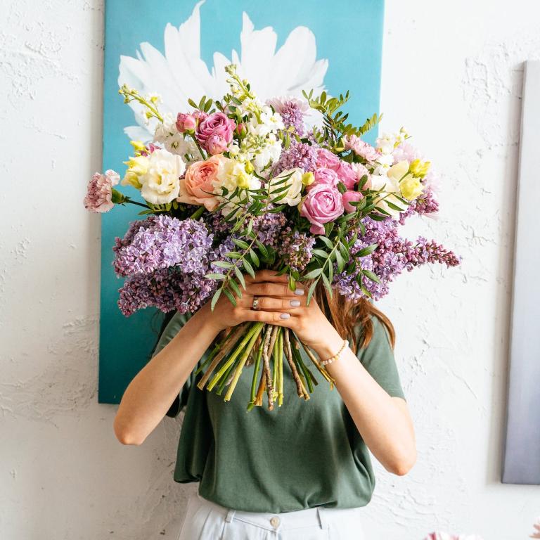 Eine Frau steht vor Gemälden und hält sich einen Blumenstrauß vor das Gesicht.