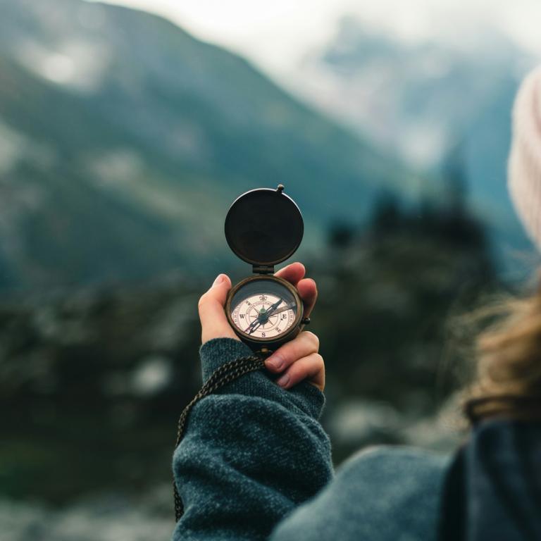 Eine Frau hält einen Kompass vor sich, im Hintergrund ist eine Berglandschaft