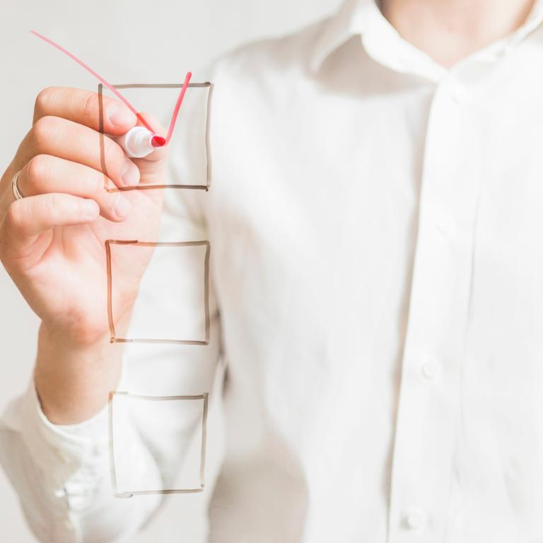 Man sieht den Oberkörper einer Person, die ein Häkchen in eines von drei Kästchen zeichnet