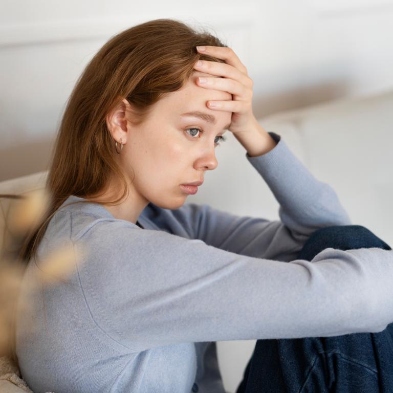 Junge Frau sitzt auf einem Sofa und schaut traurig.