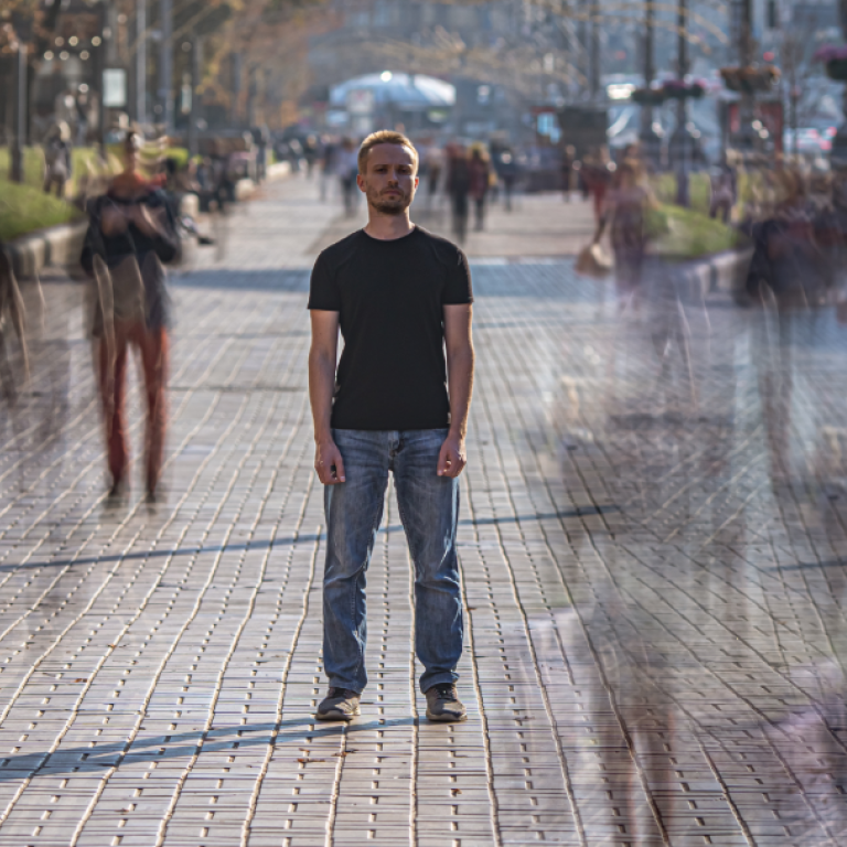 mann auf einer straße alleine, menschen um ihn herum als schatten