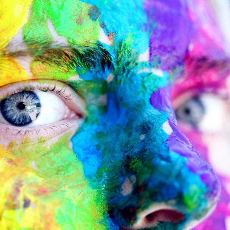 Nahaufnahme eines regenbogenfarben angemalten Gesichts einer Person mit blauen Augen.
