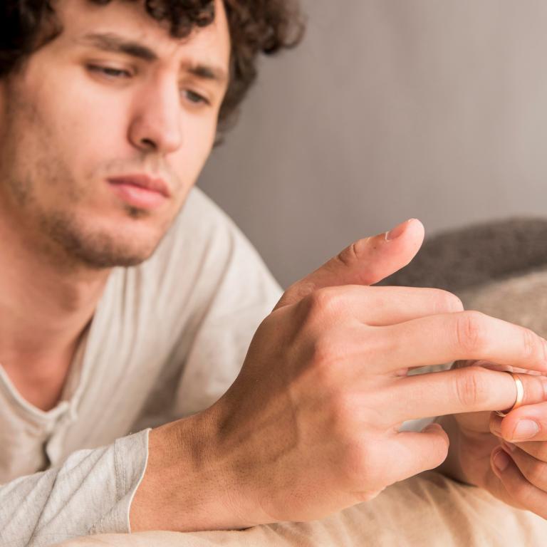 Ein Mann sitzt nachdenklich auf einem Sofa und zieht sich den Ring vom Finger