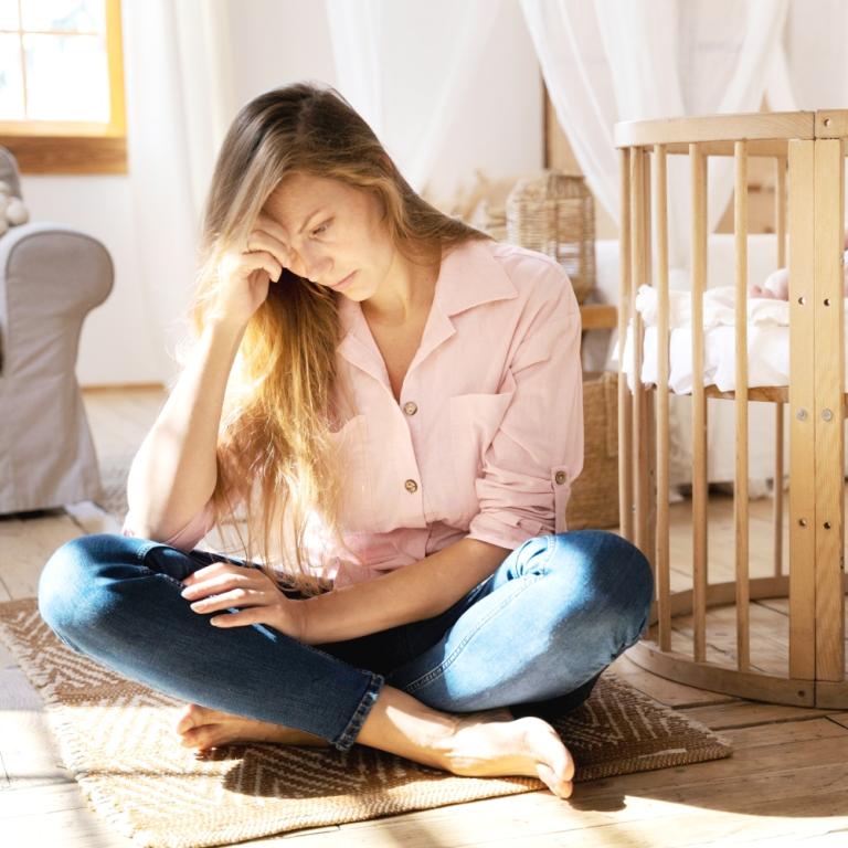 Eine junge Mutter hockt neben dem Kinderbett und liest.