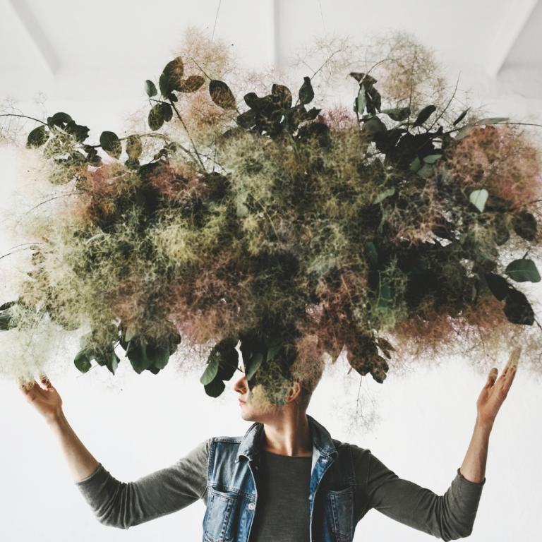 Eine Person, über und auf deren Gesicht ein Pflanzenwirrwarr schwebt