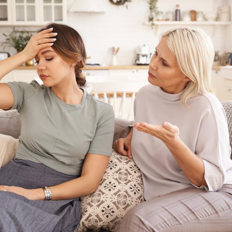Eine junge und eine mittelalte Frau sitzen nebeneinander auf einem Sofa und unterhalten sich angestrengt.