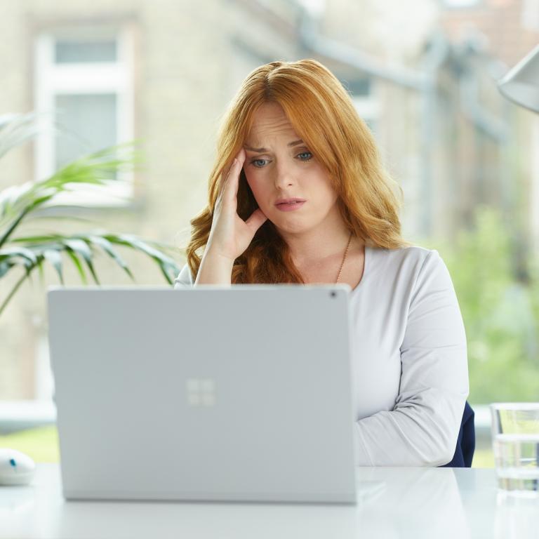 Eine junge Frau sitzt mit besorgtem Gesichtsausdruck vor einem Laptop.