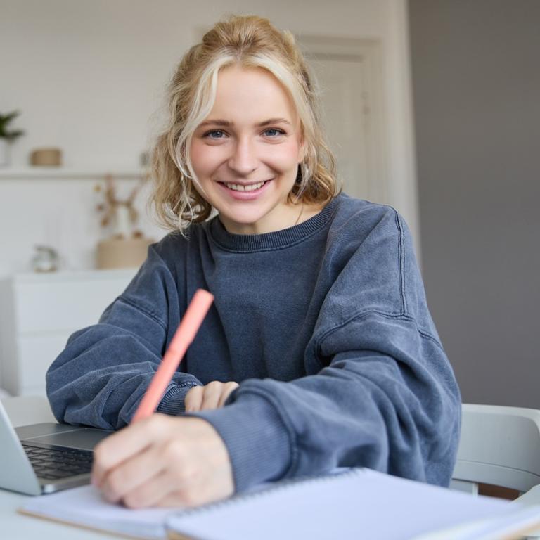Eine junge Frau sitzt am Schreibtisch und schreibt.