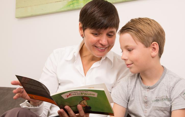 (Foto: Sandra Püttmann) Therapeutin schaut gemeinsam mit einem Jungen ein Bilderbuch an.
