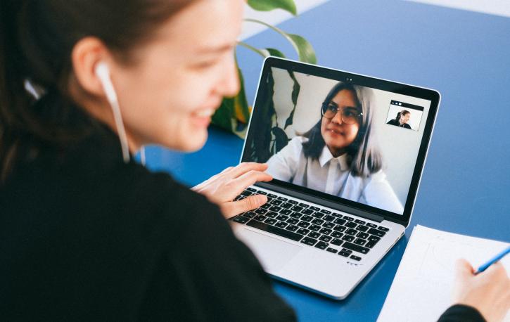 Frau sitzt lächelnd vor ihrem Laptop und spricht gerade mit einer anderen Frau per Videochat.