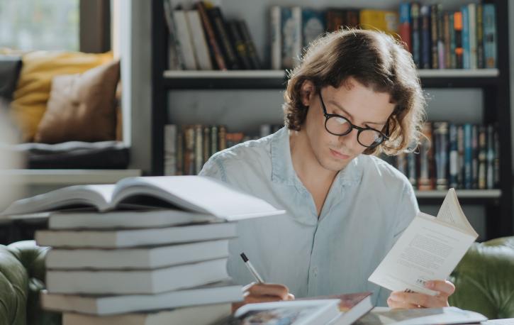 Mann mit Buch in der Hand am Schreibtisch, Stapel Bücher