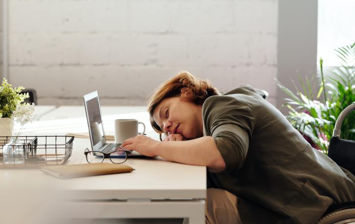 Frau schläft vor Laptop am Schreibtisch