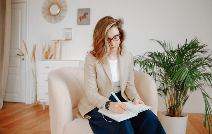 (Foto: Polina Zimmermann – Pexels.com) Blonde Frau sitzt auf einem Sessel und schreibt in ein Buch.
