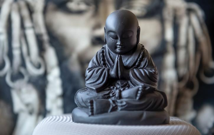 Ein kleiner Steinbuddha sitzt vor einem Bild.