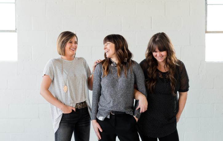 Drei jüngere Frauen stehen lässig nebeneinander und lachen.