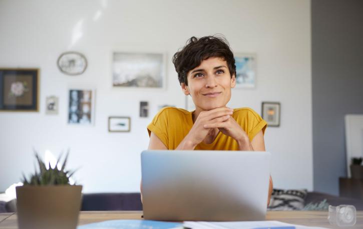 Eine Frau mit kurzen Haaren und freundlichem Gesichtsausdruck sitzt am Schreibtisch vor ihrem Laptop.