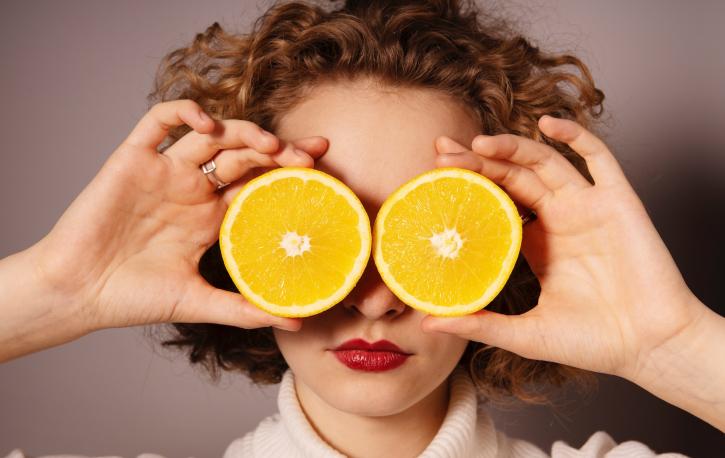 Eine Frau hält sich eine halbierte Orange vor die Augen.