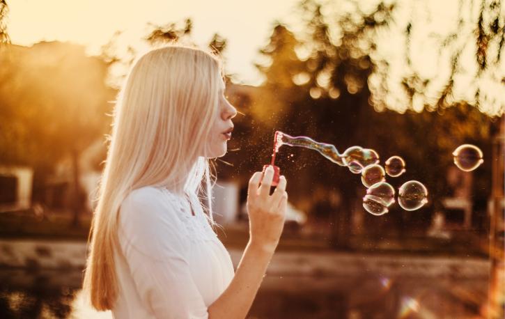 Eine Frau mit langen blonden Haaren pustet Seifenblasen in die Luft.