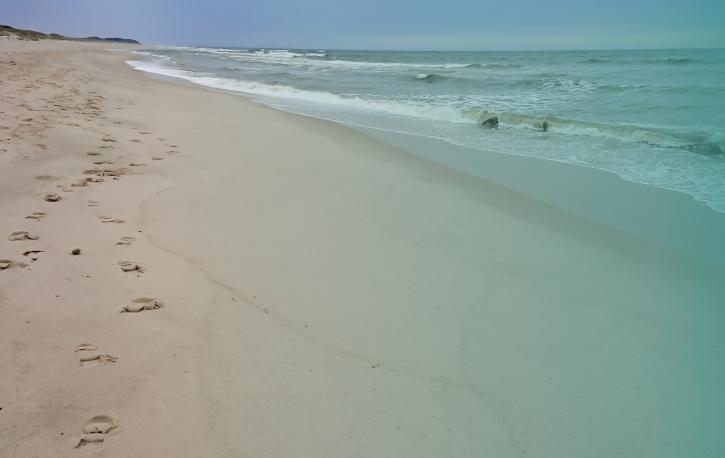 Sandstrand mit leichten Wellen rechts