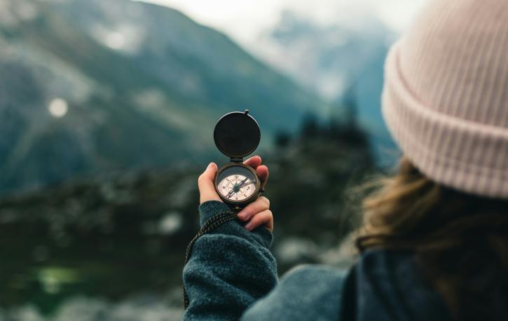 Eine Frau hält einen Kompass vor sich, im Hintergrund ist eine Berglandschaft