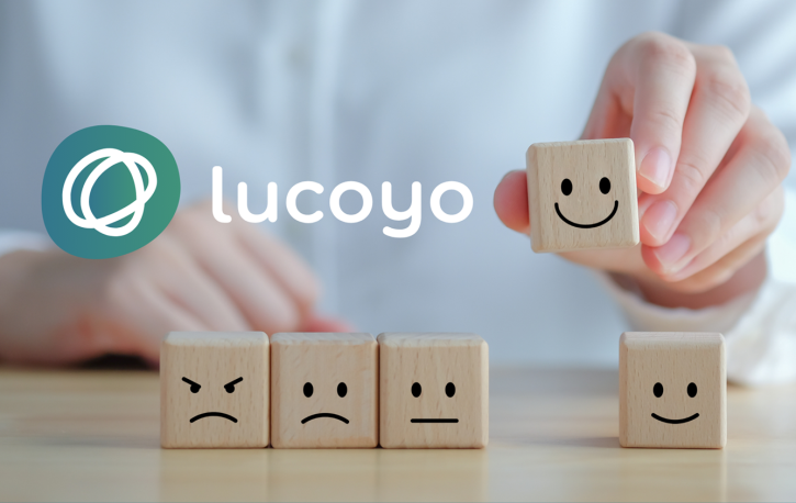 Logo von Lucoyo, darunter fünf Steinchen mit aufgemalten Gesichtern. Der lachende Stein wird hochgehalten.