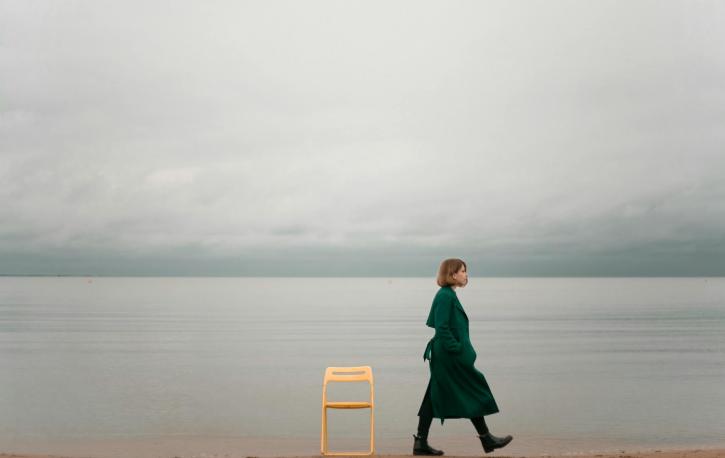 Eine Frau läuft einen leeren Strand entlang, vor dem Meer steht ein gelber leerer Stuhl