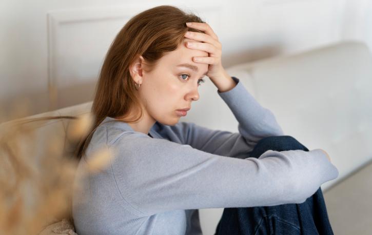 Junge Frau sitzt auf einem Sofa und schaut traurig.