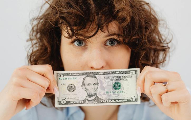 Eine brünette Frau hält sich einen Dollarschein vor das Gesicht.