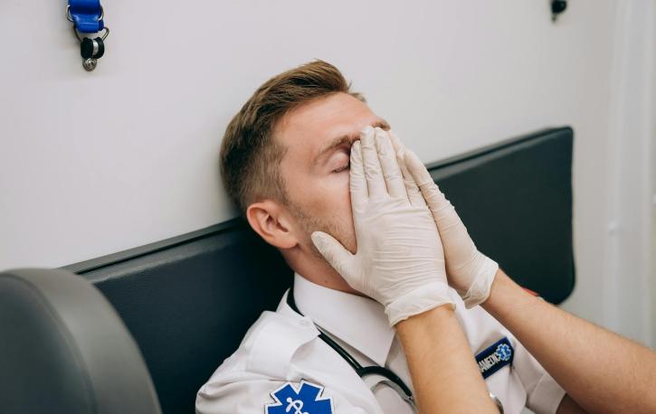 Ein Mann mit Hygienehandschuhen legt sich müde die Hände aufs Gesicht.