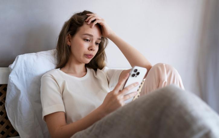 Eine junge Frau schaut sitzend auf ihr Smartphone