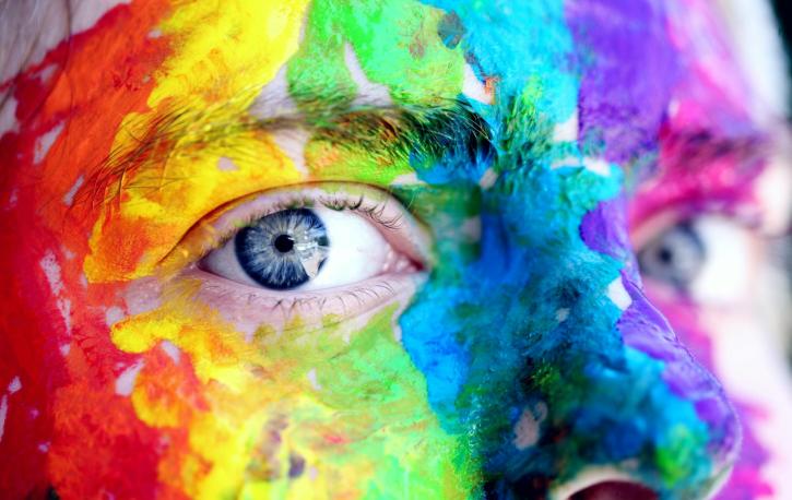 Nahaufnahme eines regenbogenfarben angemalten Gesichts einer Person mit blauen Augen.