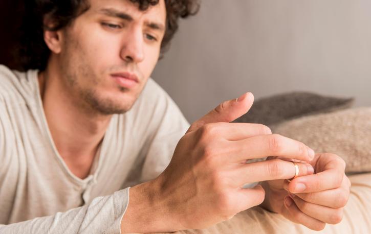 Ein Mann sitzt nachdenklich auf einem Sofa und zieht sich den Ring vom Finger