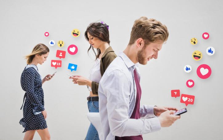 2 Frauen und ein Mann, die auf Ihre Smartphones schauen, von denen Emojis hochsteigen.