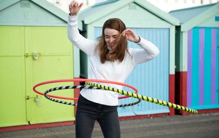 Eine Frau balanciert vor bunten Häusern mit drei Hulahoop-Reifen
