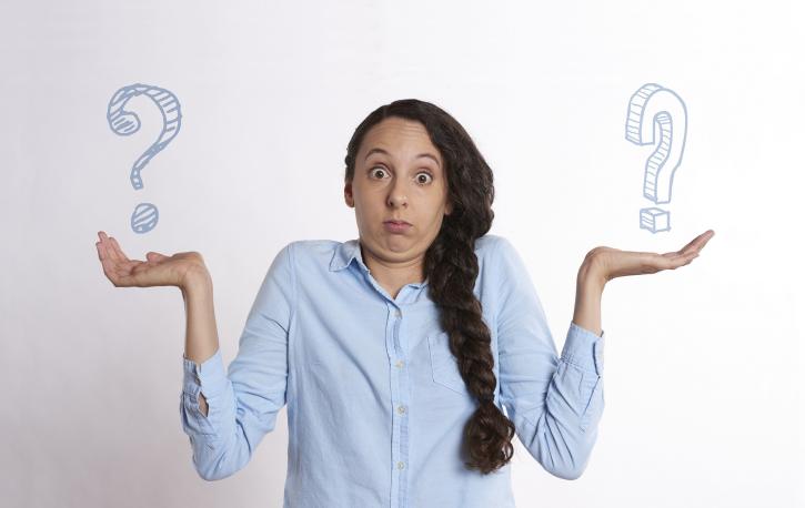 Eine Frau zieht die Schultern hoch und hebt die Hände, über deren Flächen je ein Fragezeichen schwebt