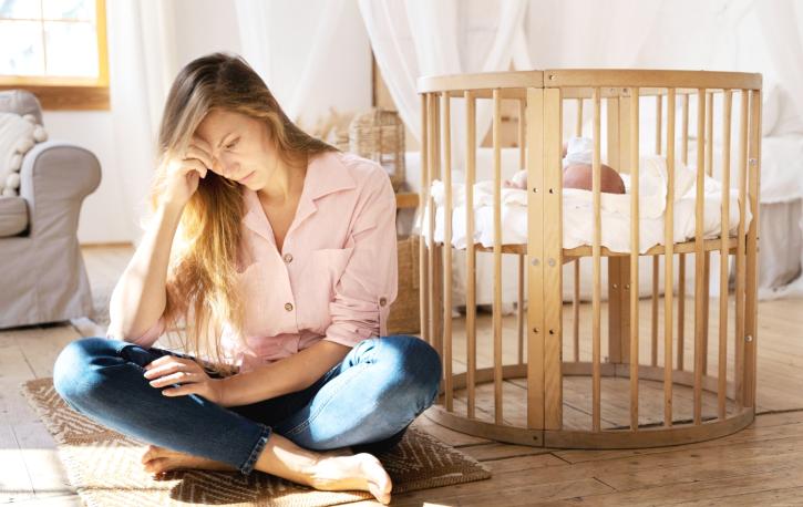 Eine junge Mutter hockt neben dem Kinderbett und liest.