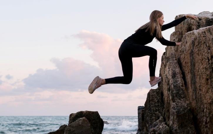 Eine Frau klettert einen Felsen am Meer hoch.