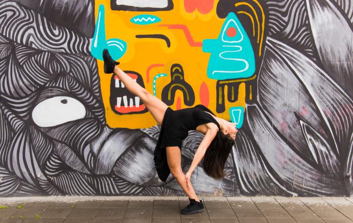 Eine Frau nimmt vor einer bunt bemalten Wand eine tänzerische Pose ein.