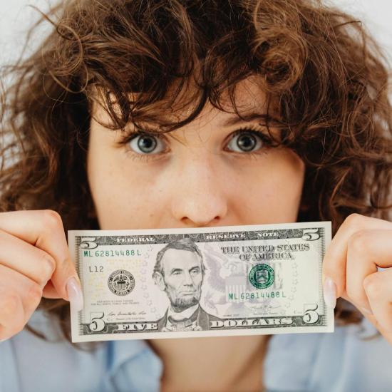 Eine brünette Frau hält sich einen Dollarschein vor das Gesicht.