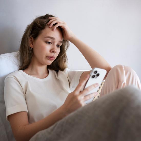 Eine junge Frau schaut sitzend auf ihr Smartphone