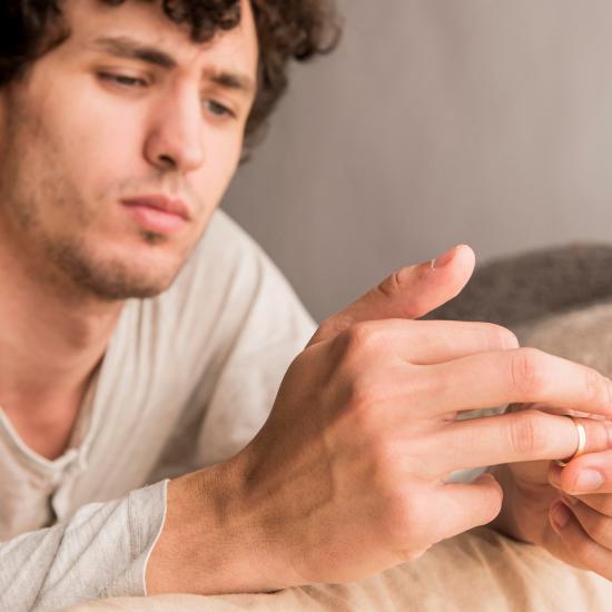 Ein Mann sitzt nachdenklich auf einem Sofa und zieht sich den Ring vom Finger