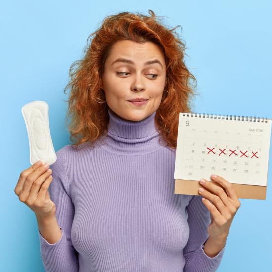 Eine Frau hält eine Binde und einen Zykluskalender in der Hand und schaut skeptisch.