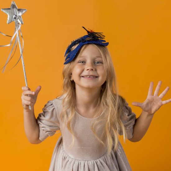 Ein kleines Mädchen mit Zauberkostüm vor orangenem Hintergrund