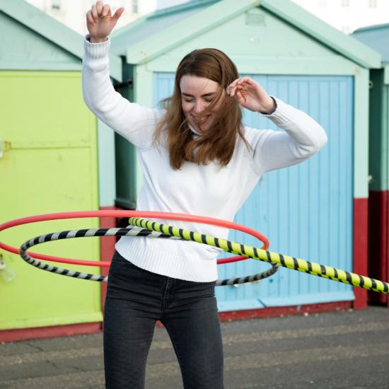 Eine Frau balanciert vor bunten Häusern mit drei Hulahoop-Reifen