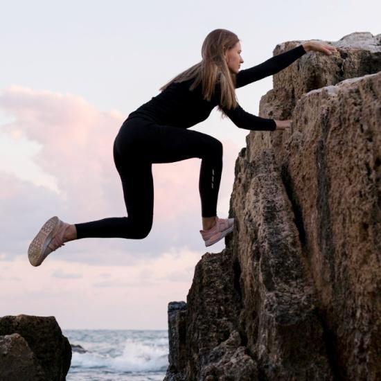 Eine Frau klettert einen Felsen am Meer hoch.