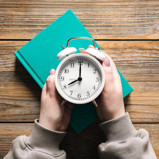 Man sieht einen weißen Wecker von oben, der von zwei Händen umfasst wird.