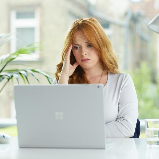 Eine junge Frau sitzt mit besorgtem Gesichtsausdruck vor einem Laptop.